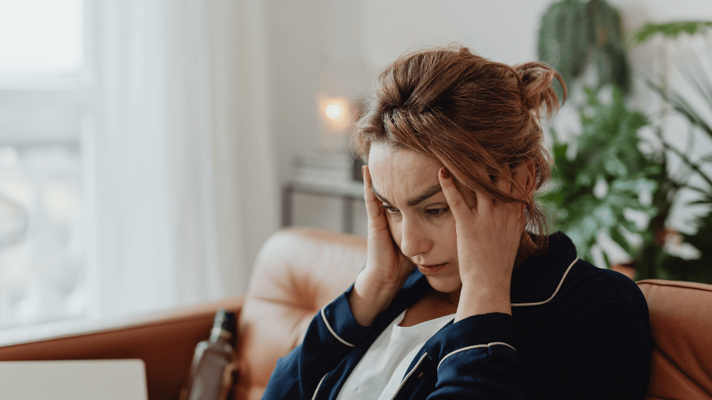 Person sitting on a couch holding their head while feeling overwhelmed and stuck in overthinking during an important decision