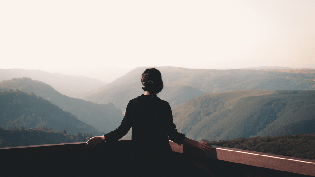 Person reflecting on a difficult life decision while looking out over a mountain landscape